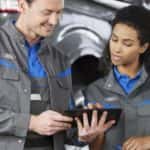Ford technicians are shown near a vehicle on a lift at an auto repair shop.