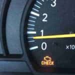 A close up of a vehicle's dashboard displaying a check engine light.
