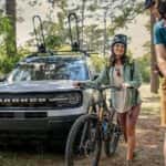 Two people with bikes are walking away from a white 2023 Ford Bronco Sport.