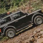 A black 2025 Ford Bronco Base is off-roading on a steep rocky trail.