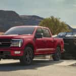 A red 2024 Ford F-150 Platinum towing a boat at a lake.