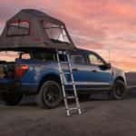 A blue 2025 Ford F-150 is parked at a remote campsite during a sunset.