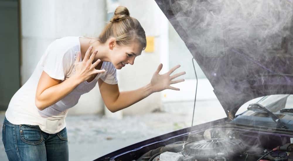 A person in shown standing over an overheated engine.