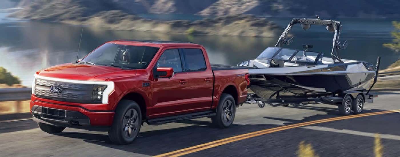 A red 2025 Ford F-150 Lightning towing a boat.