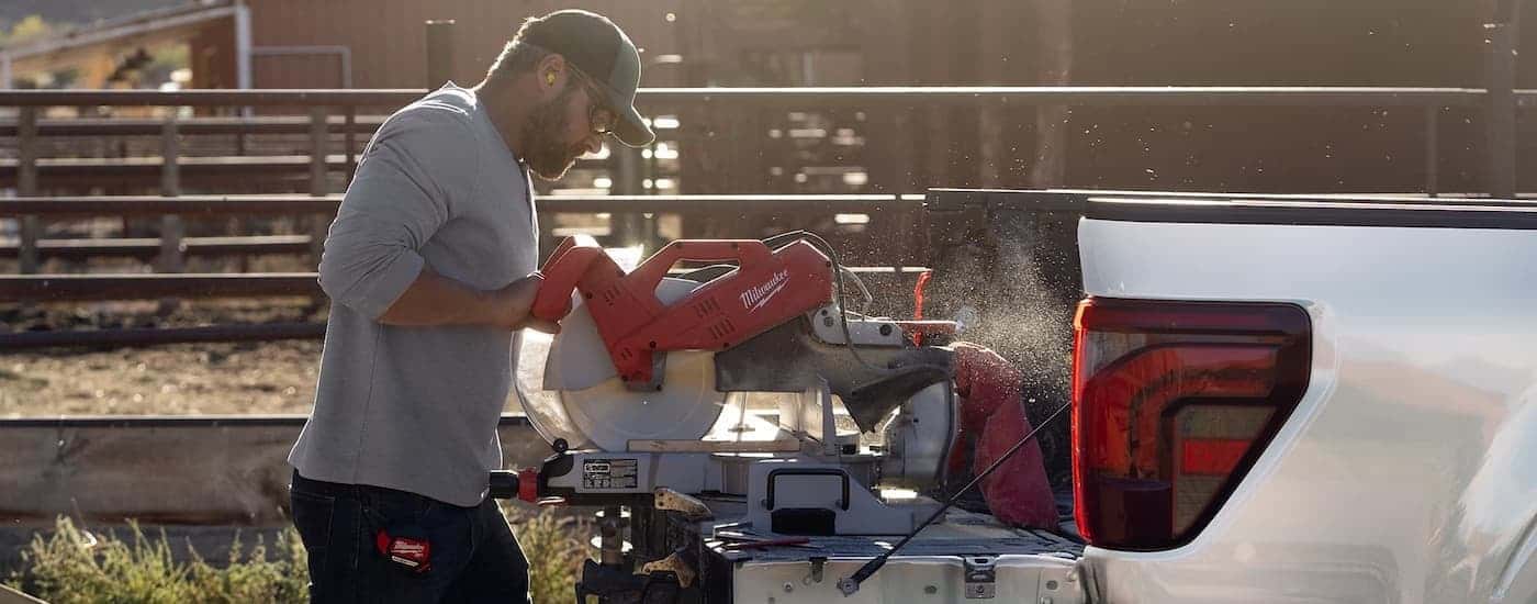 A person using an electric saw on the tailgate of a white 2025 Ford F-150.