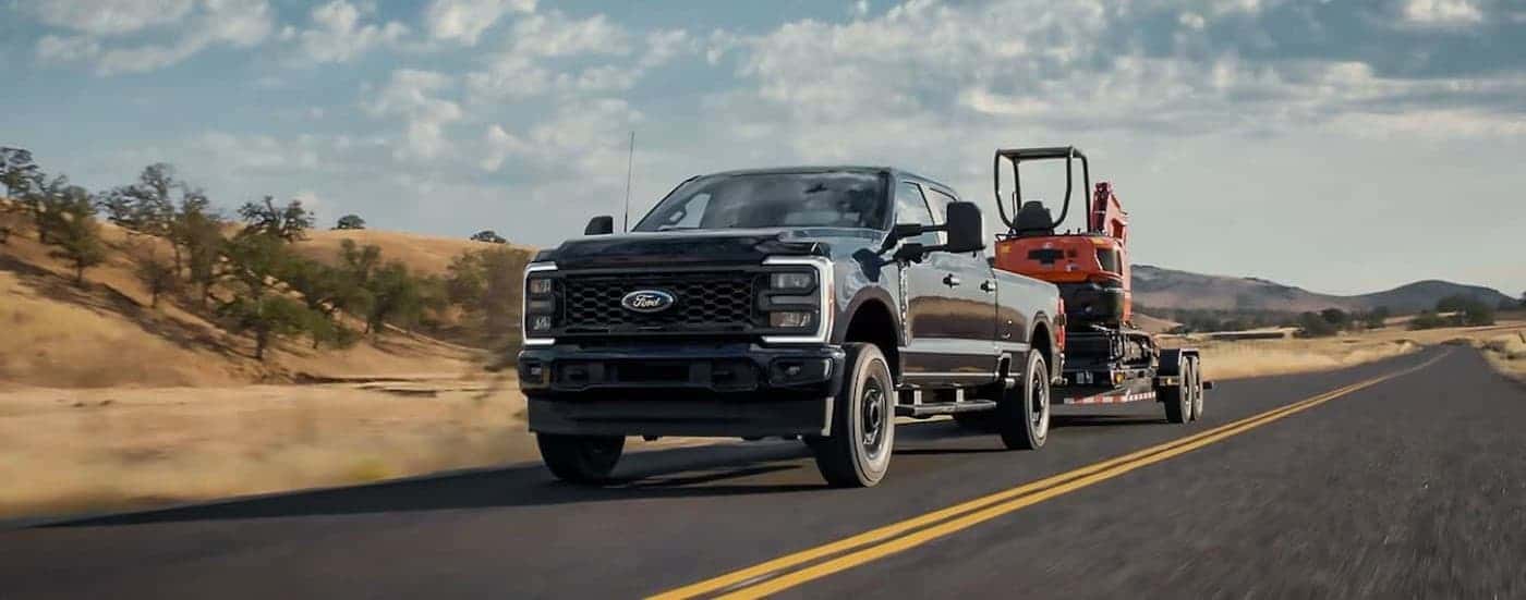 A black 2025 Ford F-350 towing a trailer on a highway.
