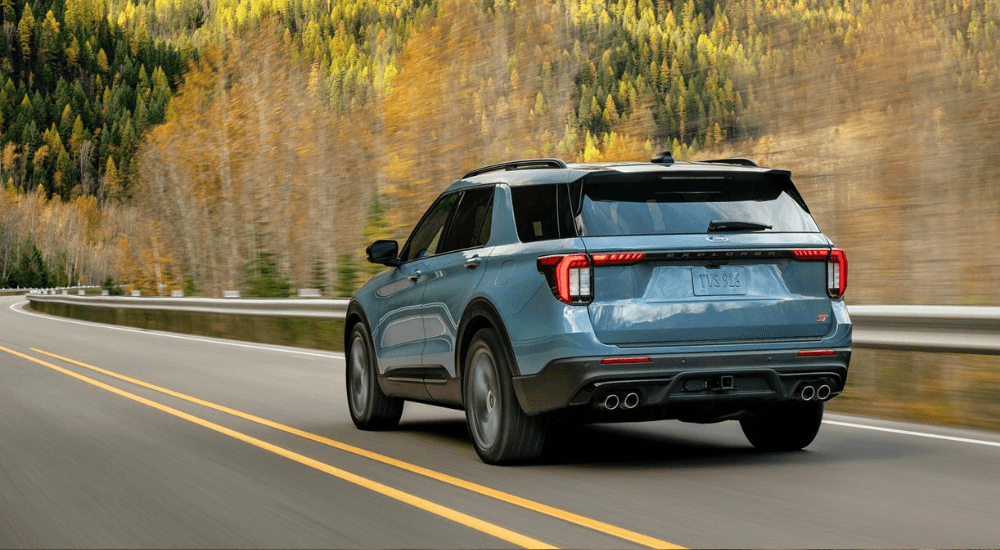 Blue 2026 Ford Explorer driving down woodland road from the back at an angle.