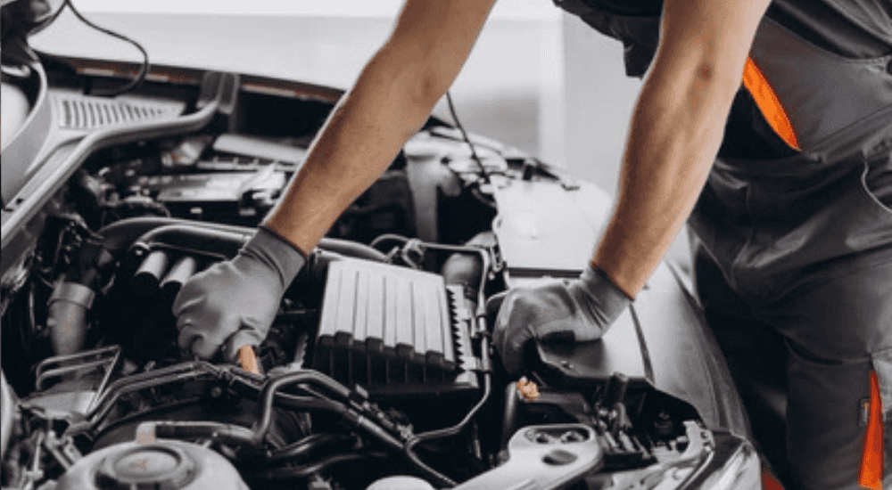 A car tech works under the hood of a car showing transmission rear near Snellville.