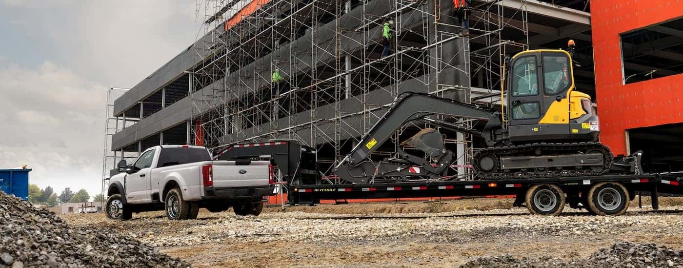 A white 2026 Ford F-450 towing heavy machinery.