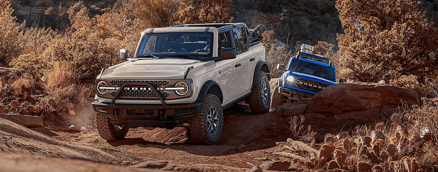 A white 2026 Ford Bronco driving down a trail with a blue one following