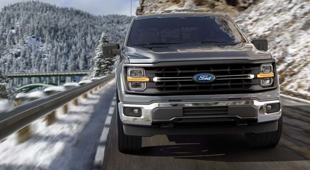 A gray Ford F-150 Lariat driving on a snow-lined mountain roadway.