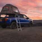 A person tending a fire next to a blue Ford F-150 STX FX4 with a tent accessory.