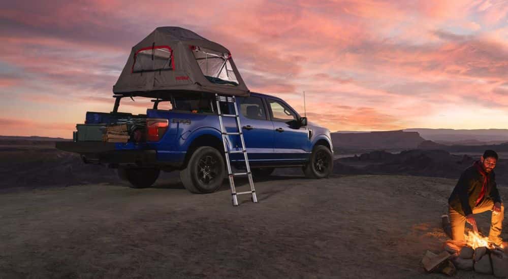 A person tending a fire next to a blue Ford F-150 STX FX4 with a tent accessory.