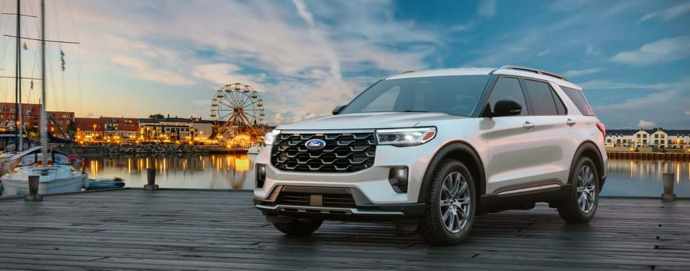 A silver 2026 Ford Explorer® SUV parked on a pier near an amusement park.