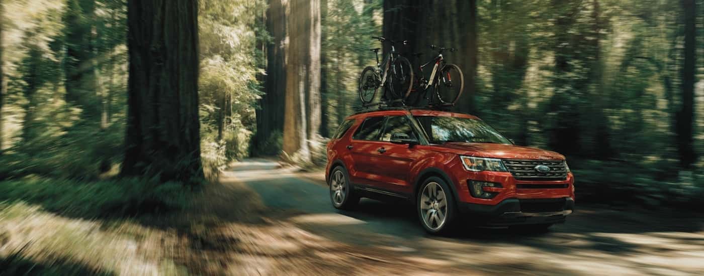 Red 2016 Ford Explorer driving on a tree-lined trail
