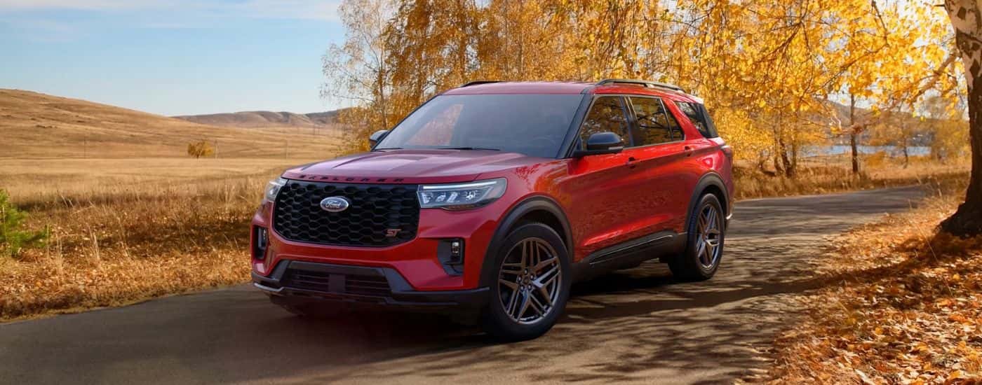 A red 2026 Ford Explorer ST shown driving an autumn tree-lined road.