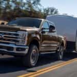 Brown 2026 four door Ford F-250 twoing a trailer down a paved road.