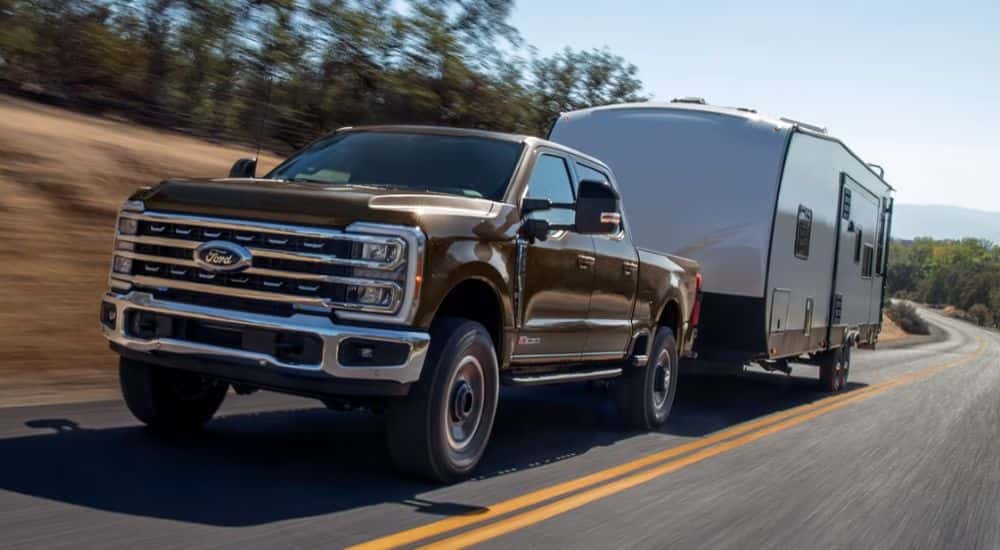 Brown 2026 four door Ford F-250 twoing a trailer down a paved road.