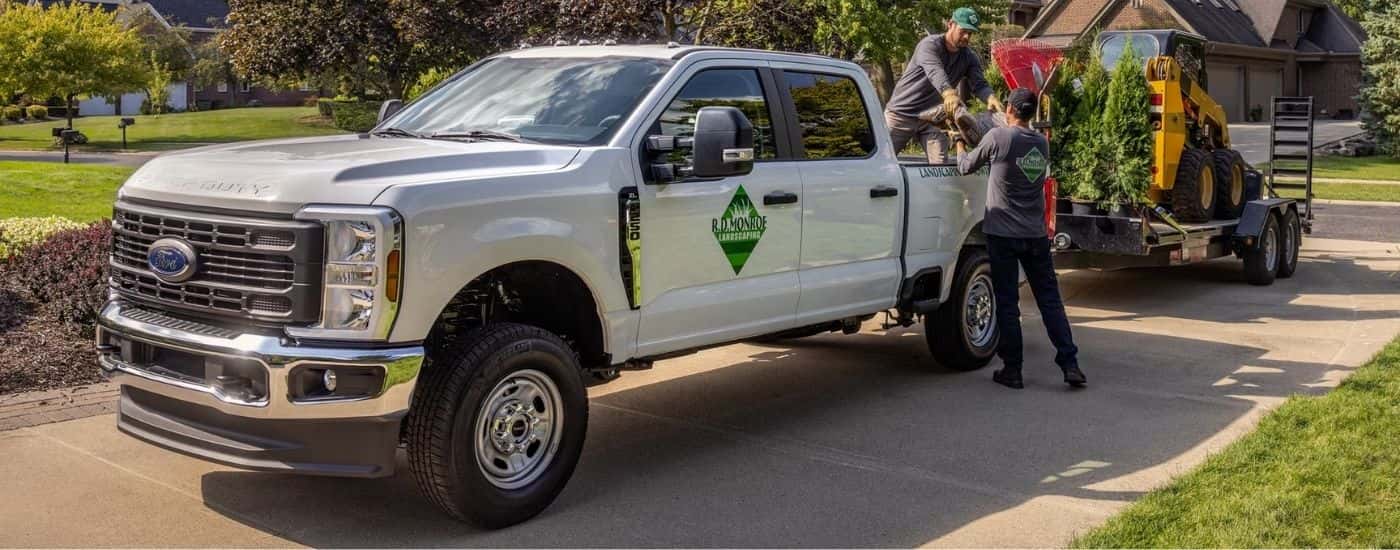 A white 2026 Ford F-250 Super Duty towing landscaping equipment.