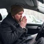 A modern young man in his car rubbing and blowing his hand so he can warm up himself