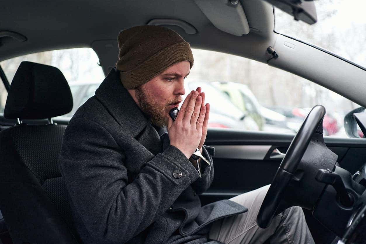 A modern young man in his car rubbing and blowing his hand so he can warm up himself