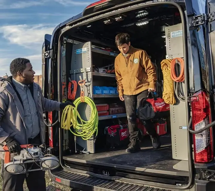 a worker handing equipment to his co-worker who is standing inside the back of an e-transit