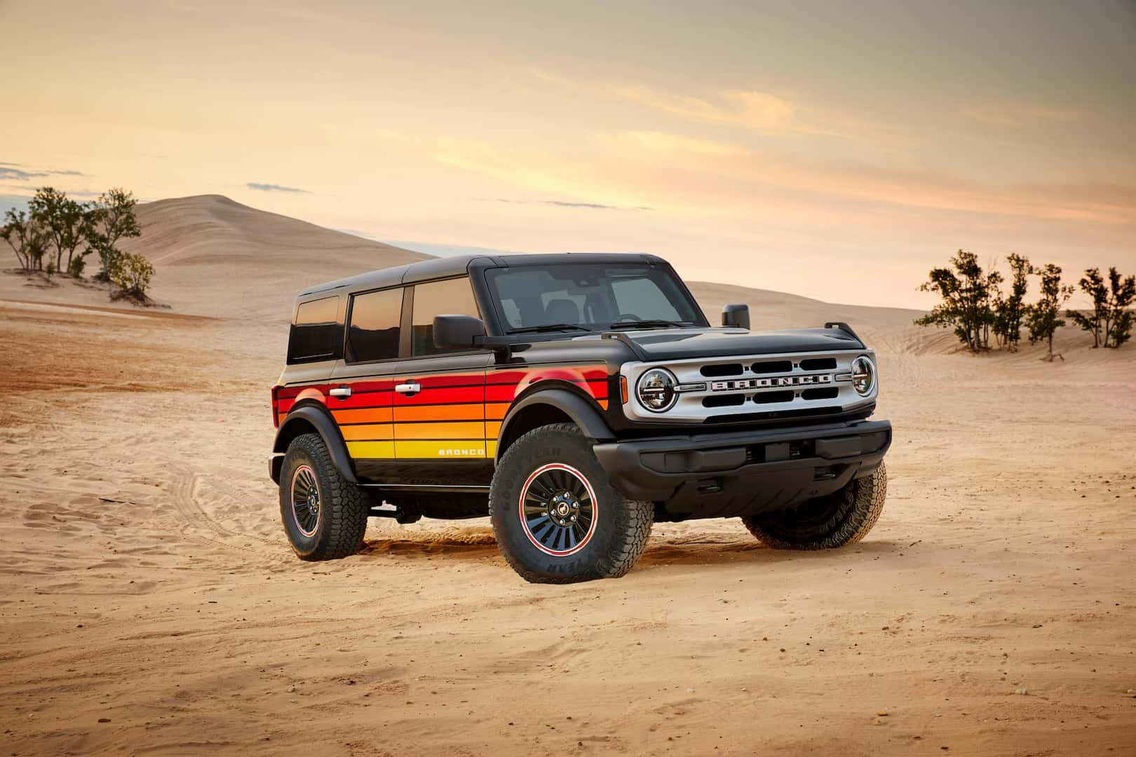 a black ford bronco with red to yellow gradient stripes free wheeling on desert road