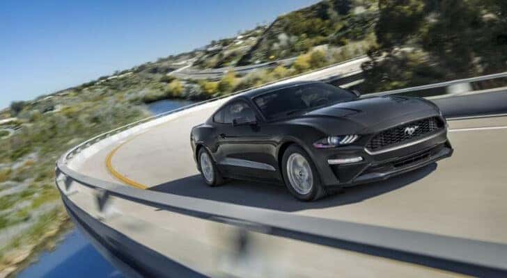 A black 2023 Ford Mustang driving to a Ford dealer.