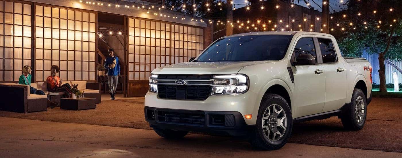 A tan 2024 Ford Maverick LARIAT parked under cafe lights at night.