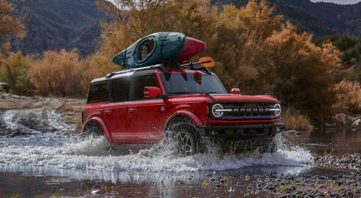 A red 2024 Ford Bronco Outer Banks driving over a shallow pond.