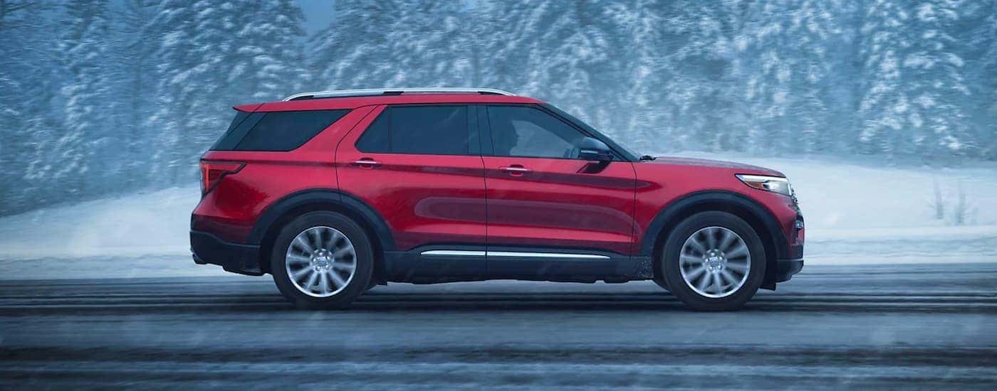 Side angle view of a red 2024 Ford Explorer Limited driving down a snowy road.