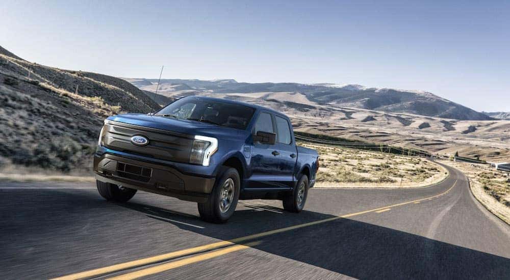 A blue 2022 Ford F-150 Lightning leaving a dealer that has a used Ford F-150 for sale.