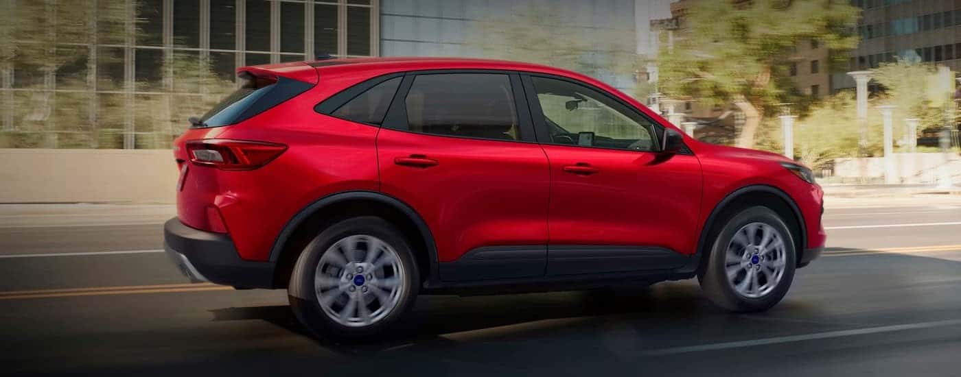 A red 2025 Ford Escape for sale is shown driving on a city street.