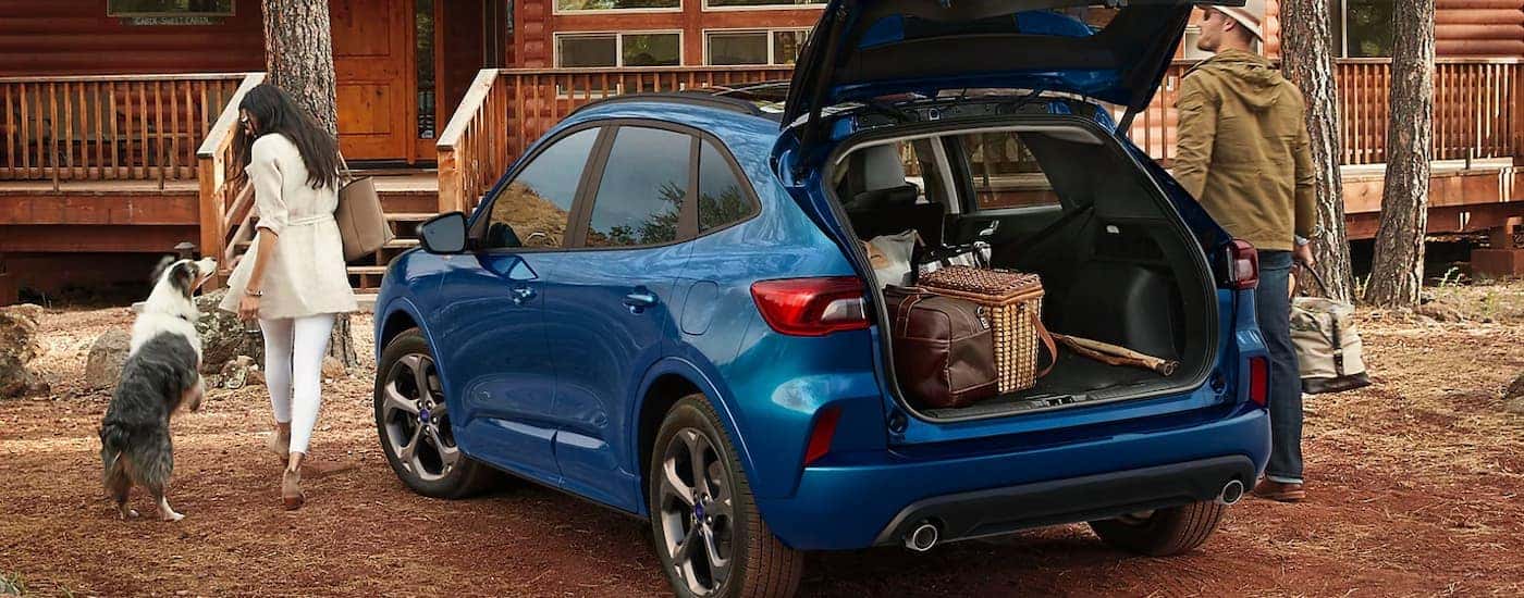 Rear view of a blue 2024 Ford Escape ST-Line with an open hatch parked in front of a house.