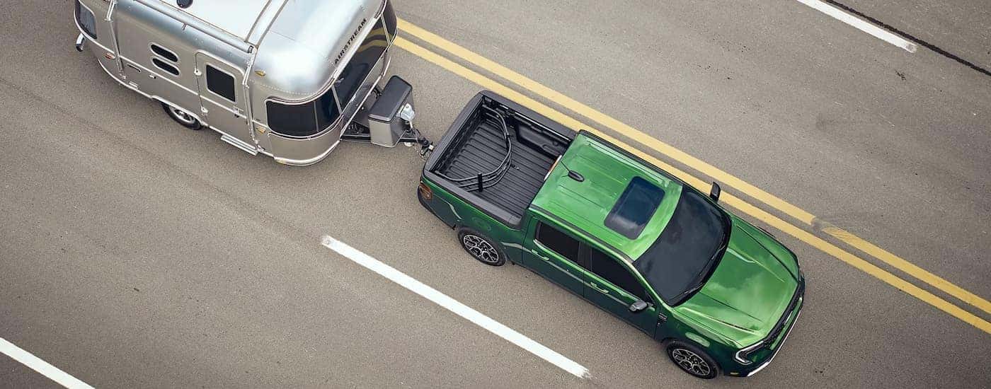 Green 2025 Ford Maverick towing a silver camper.