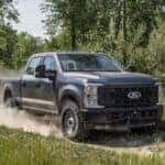 A gray 2025 Ford F-250 for sale driving on a dirt path.