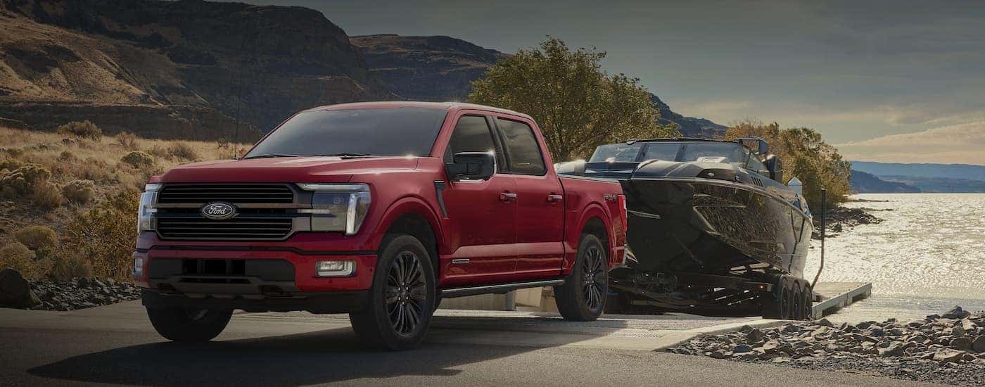Red 2025 Ford F-150 STX towing a boat out of a lake.