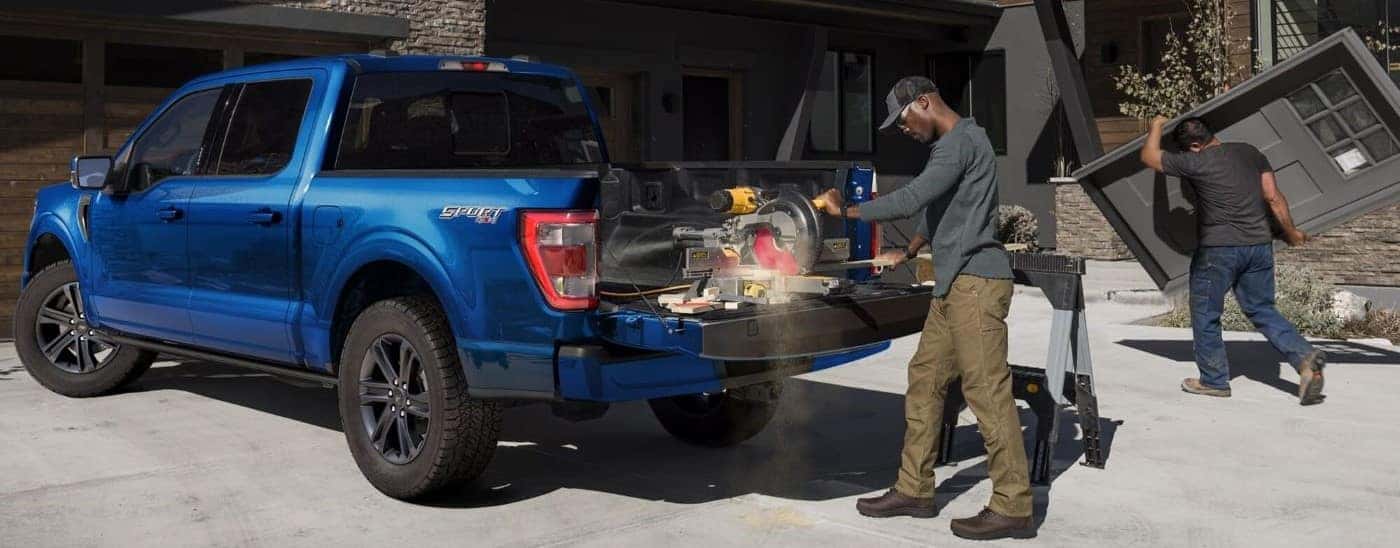 A person uses a saw on the tailgate of a blue 2023 Ford F-150 Sport