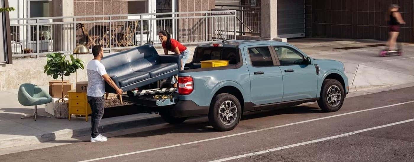 Two people loading a couch into a blue 2022 Ford Maverick