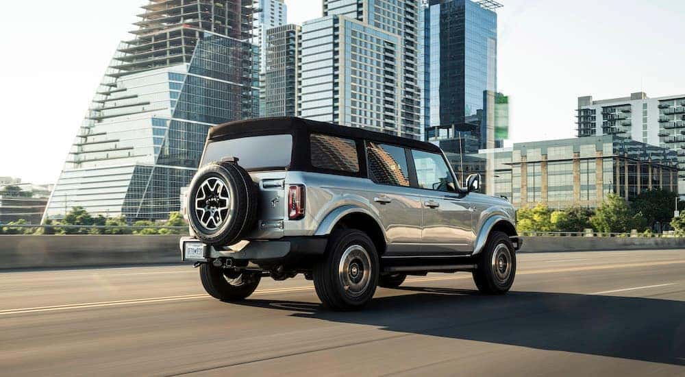 A silver 2021 Ford Bronco Outer Banks is driving past city buildings.