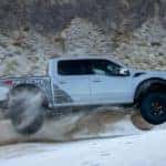 A silver 2023 Ford F-150 Raptor R is shown from the side while jumping over a sand dune.