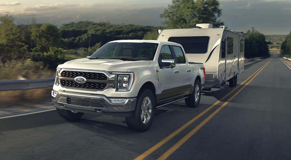 A white 2023 Ford F-150 is towing a trailer on an open road.