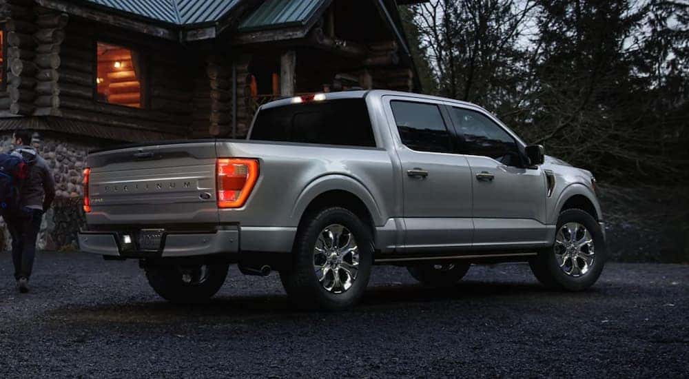 A grey 2023 Ford F-150 for sale is parked in front of a log cabin.