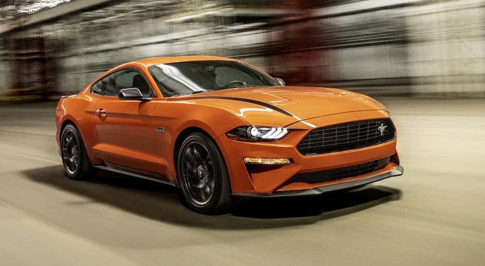 An orange 2021 Ford Mustang Ecoboost HPP is driving past scaffolding.