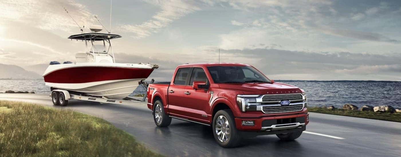 A red 2024 Ford F-150 Platinum is shown towing a boat near water.