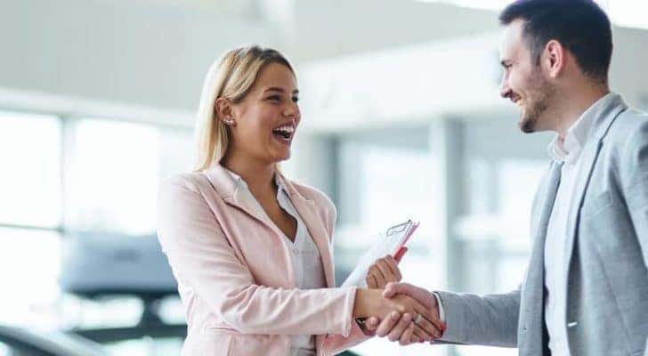 A salesperson is shaking hands and smiling with a customer at a Ford dealer near you.