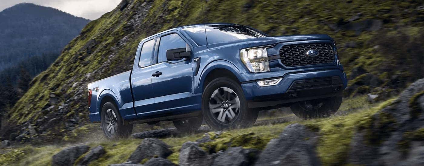 A blue 2023 Ford F-150 STX is driving on a steep rocky mountain road.