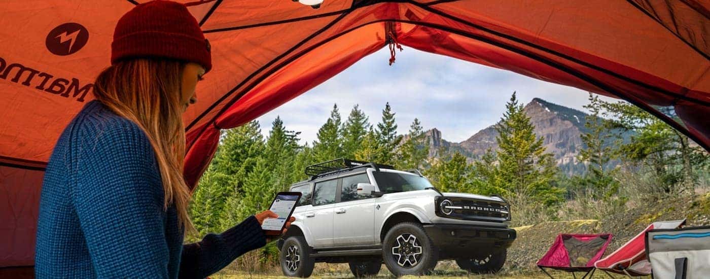 A white 2022 Ford Bronco Outer Banks is shown parked near a person in a tent.