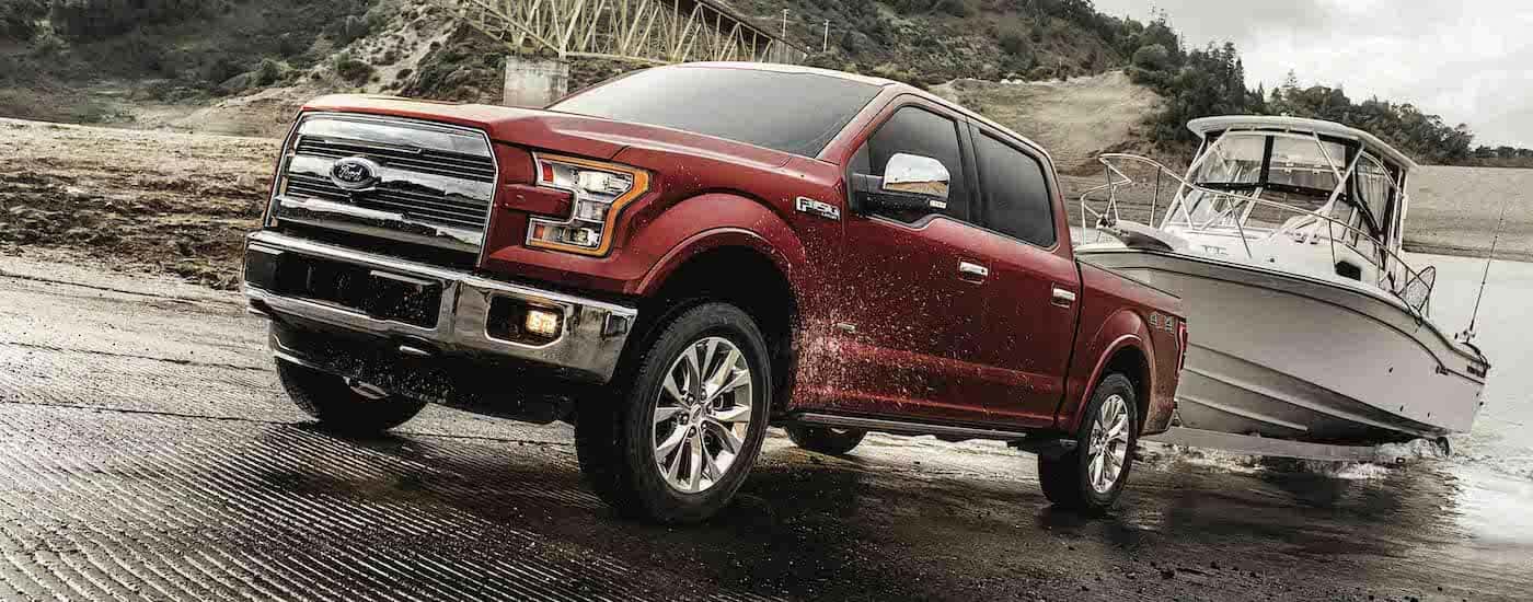 A red 2017 Ford F-150 is towing a fishing boat out of lake.