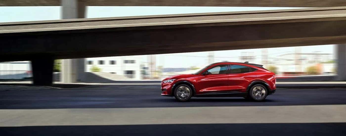 A red 2022 Ford Mustang Mach-E is driving past an onramp.